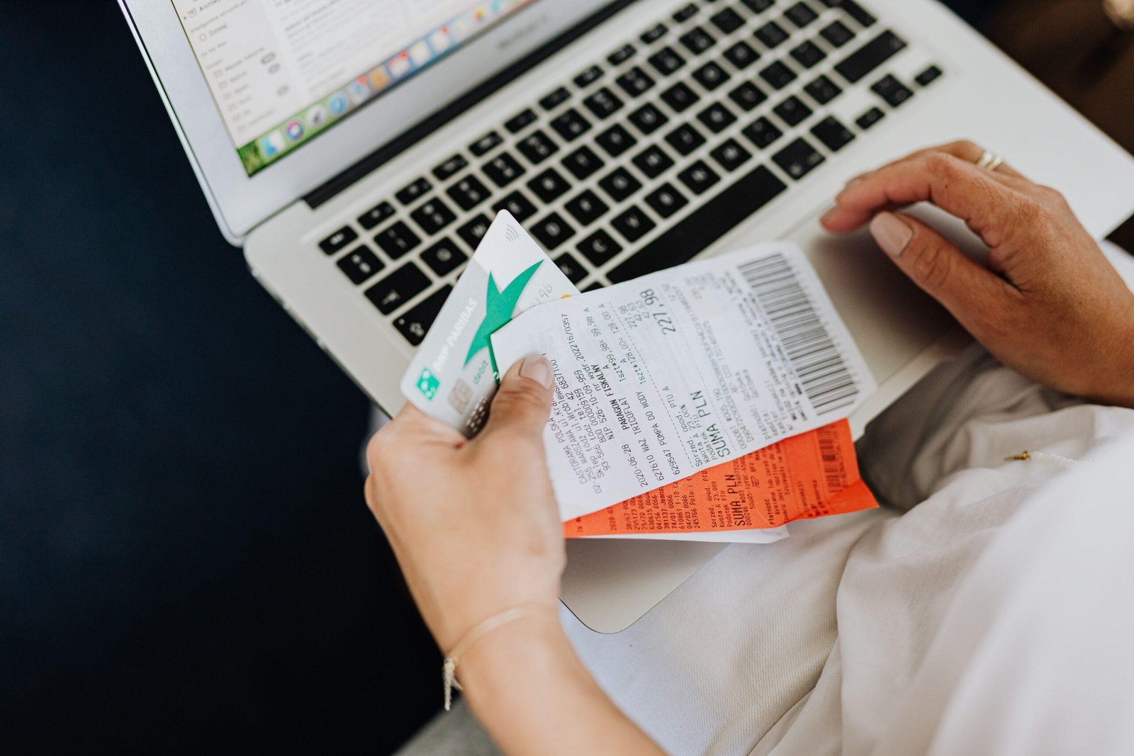 Person reconciling online sales with a credit card and receipts at a laptop